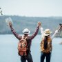 Two travelers with backpacks stand on a cliff, gazing at a serene lake below, embodying adventure and exploration.