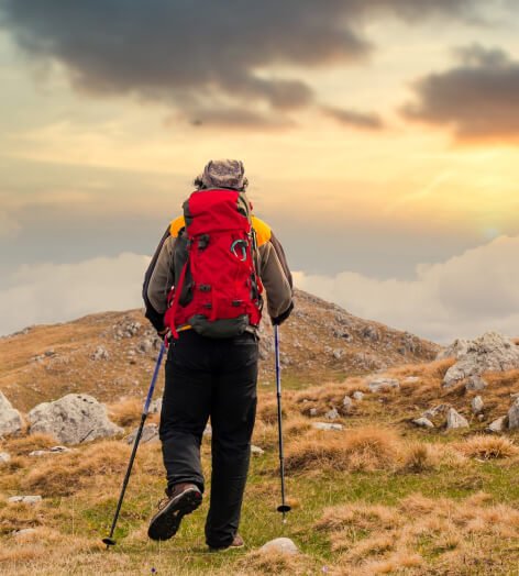 A man with a backpack and trekking poles ascends a hill, embodying the spirit of adventure in travel and exploration.